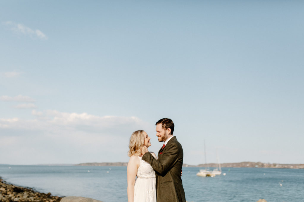 A bride and groom look at one another with Portland Harbor in the background during their Maine elopement.
