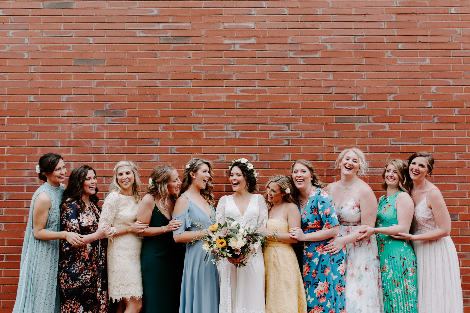 A bride and her bridesmaids in colorful dresses laugh in downtown Portland, Maine.  