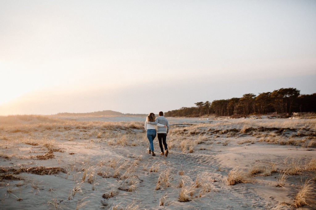 An engaged couple walks down the beach in Maine 