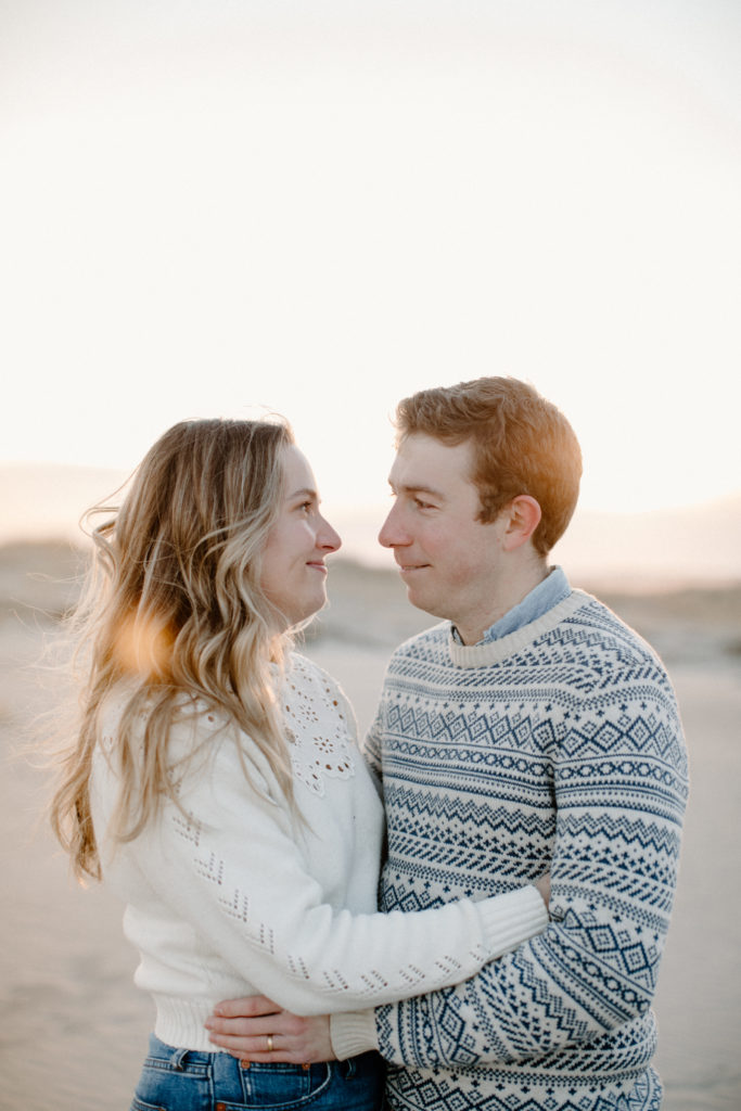 A married couple snuggles up together during golden hour on a Maine beach